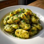 Nahaufnahme von fluffigen Gnocchi mit grünem Pesto und Sahne, bestreut mit Parmesan.