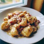 Teller mit fluffigen Gnocchi in einer cremigen Schinken-Sahne-Soße, bestreut mit schwarzem Pfeffer.