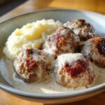 Nahaufnahme von saftigen Hackbällchen in Schmand-Sauce mit cremigem Kartoffelpüree.