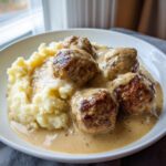 Teller mit saftigen Hackbällchen in cremiger Zwiebel-Sahnesauce und fluffigem Kartoffelstampf.