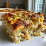 Ein saftiges Stück Hähnchen-Kartoffelgratin mit Käse auf einem weißen Teller, goldbraun überbacken.