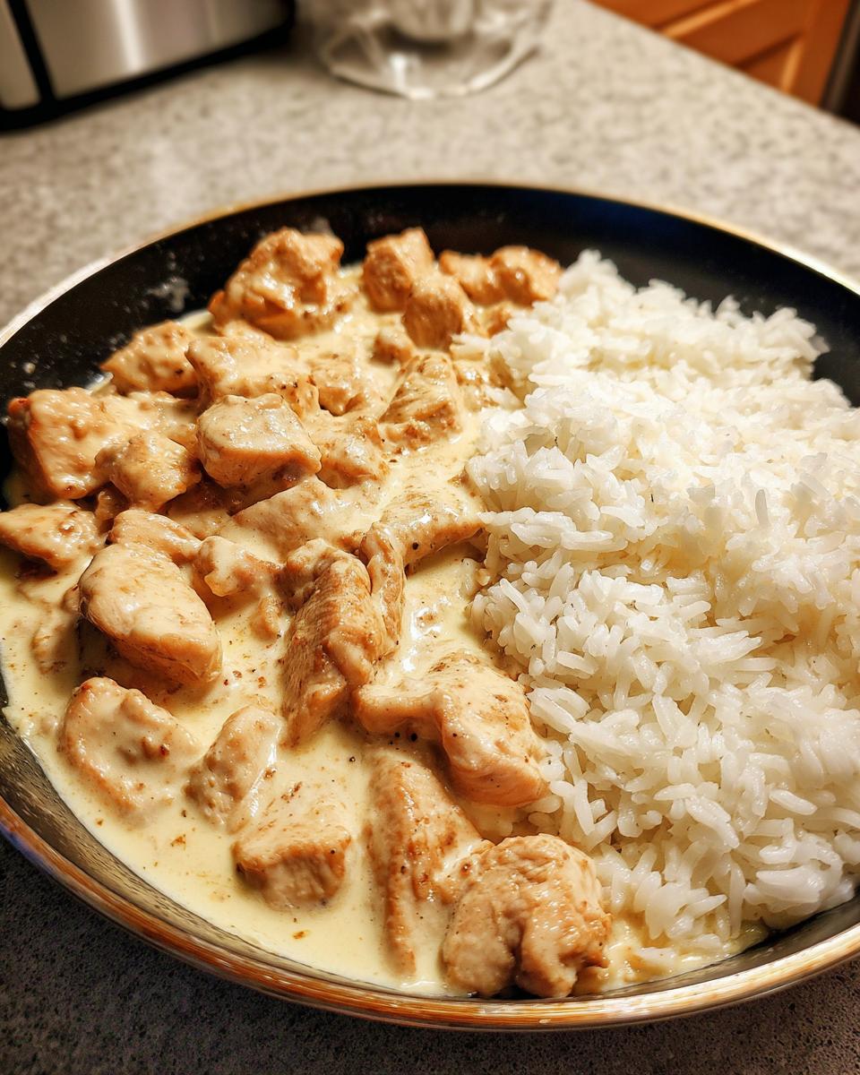 Köstliche Hähnchenpfanne in cremiger Frischkäsesauce neben lockerem Reis in einer schwarzen Pfanne.