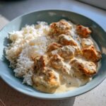 Nahaufnahme einer Hähnchenpfanne in cremiger Frischkäsesauce mit Reis auf einem hellblauen Teller.