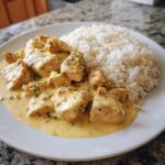 Fertige Hähnchenpfanne in Käse-Sahne mit Reis auf einem weißen Teller angerichtet.
