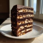 Ein hohes, anschnittfrisches Stück Kalter Hund klassisch mit vielen Schichten aus dunkler Schokolade und Butterkeksen.