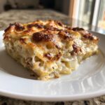 Ein saftiges Stück Kartoffelgratin mit Hähnchen in Sahnesauce auf einem weißen Teller mit goldbraun gebackener Käsekruste.