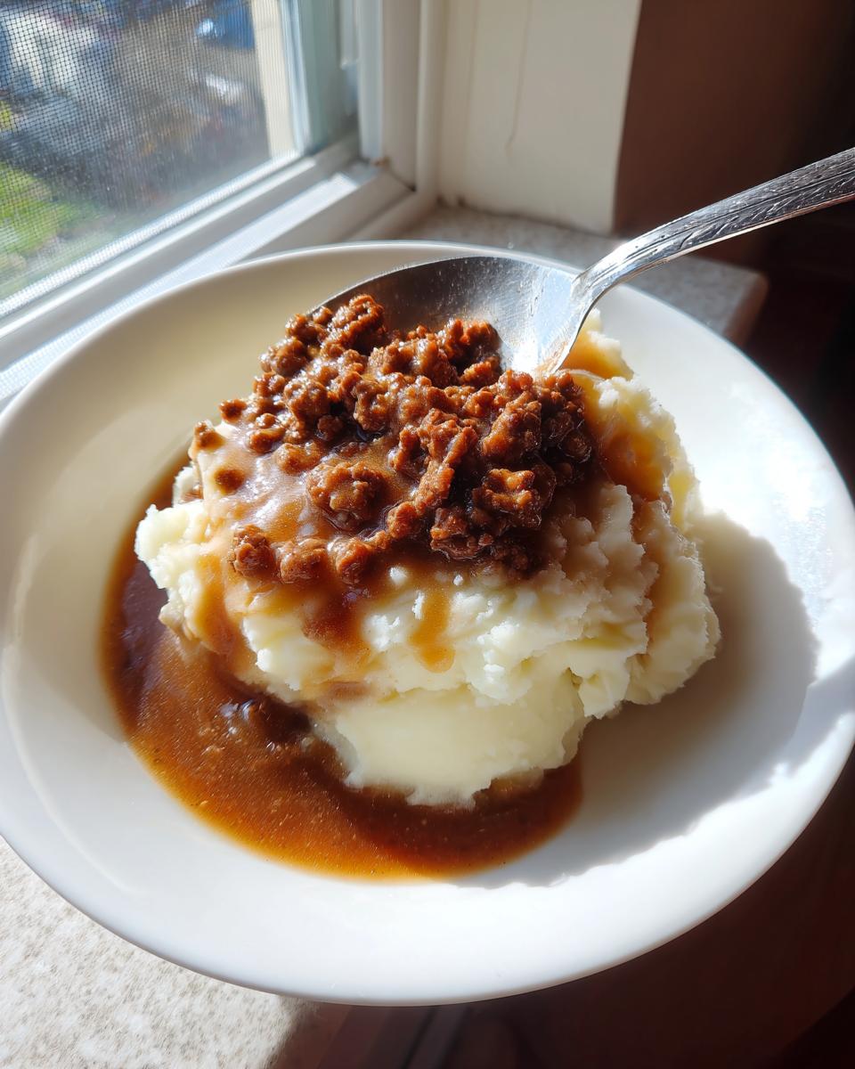 Ein Teller mit fluffigem Kartoffelpüree, bedeckt mit cremigem Hackfleisch und dunkler Bratensauce, bereit zum Essen.