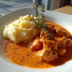 Ein Teller mit cremigem Kartoffelstampf und saftigen Hähnchenstücken in leuchtender Paprikarahm-Soße.