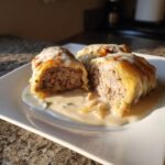 Nahaufnahme von zwei aufgeschnittenen Kohlrouladen in Rahmsauce auf einem weißen Teller.