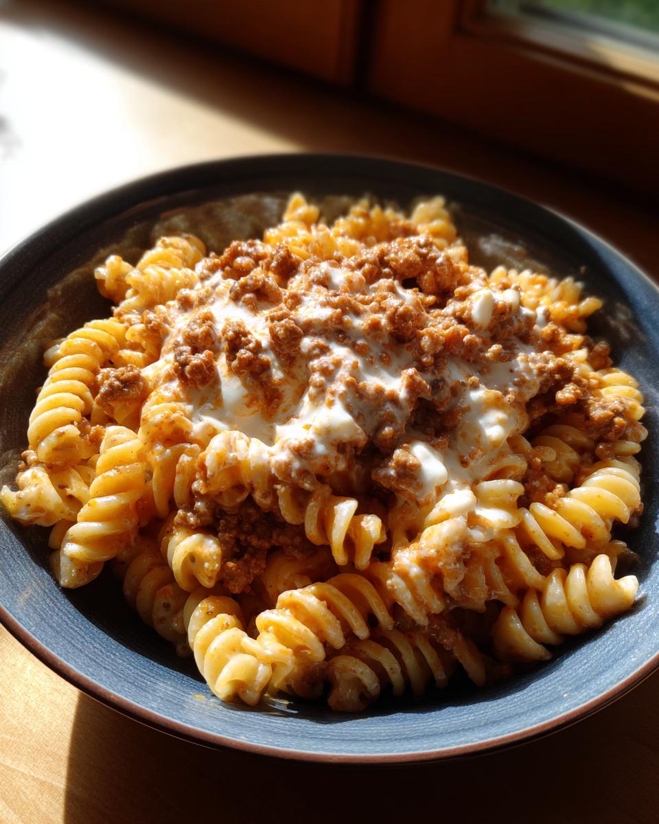 Nahaufnahme von Nudeln mit Hackfleisch und Schmand in einer dunklen Schüssel, appetitlich angerichtet.