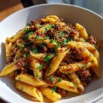 Nahaufnahme einer leckeren Nudelpfanne mit Hackfleisch und frischen Kräutern in einer weißen Schüssel.