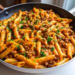 Nahaufnahme einer cremigen Nudelpfanne mit Hackfleisch und Paprikacreme, garniert mit frischer Petersilie.