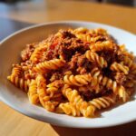 Nahaufnahme einer Portion Nudelpfanne mit Hackfleisch und Tomatenmark, serviert in einem weißen Teller.