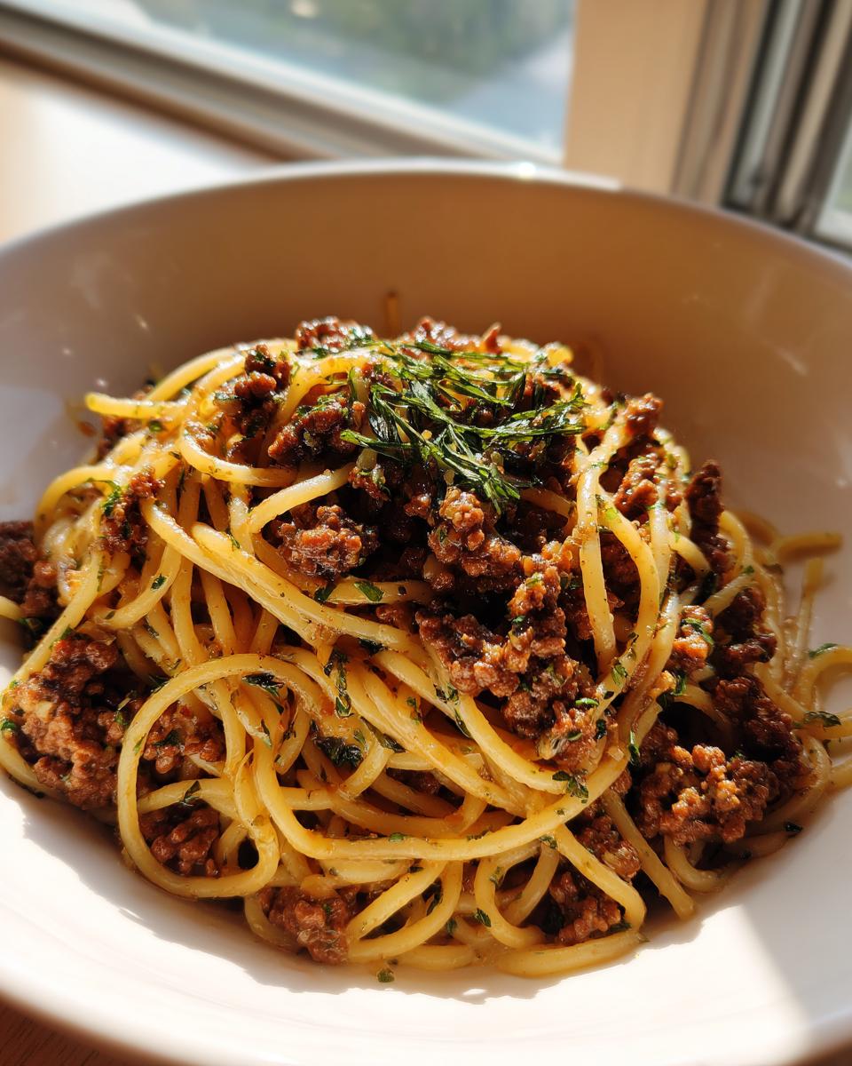 Nahaufnahme von Pasta mit Hackfleisch und Kräuterbutter in einer weißen Schüssel, appetitlich garniert.