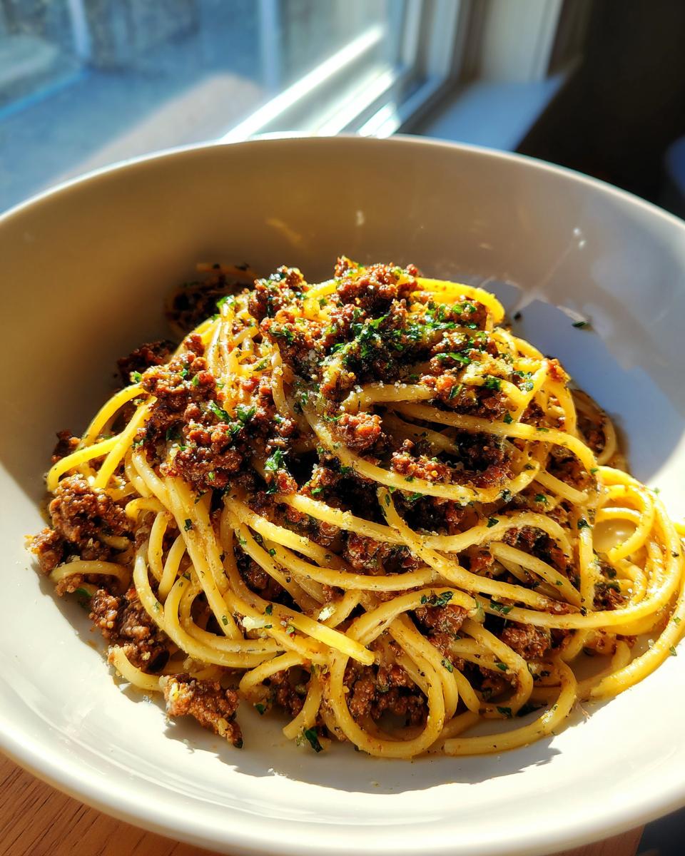 Nahaufnahme einer Schüssel Pasta mit Hackfleisch und Kräuterbutter, appetitlich angerichtet und sonnenbeschienen.