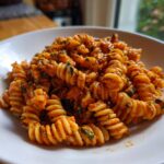 Nahaufnahme von cremiger Pasta mit Tomatenpesto und Sahne, garniert mit frischen Kräutern.