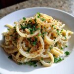 Nahaufnahme von Pasta mit Zwiebel-Sahnesauce, garniert mit gebratenen Zwiebelringen und Petersilie.