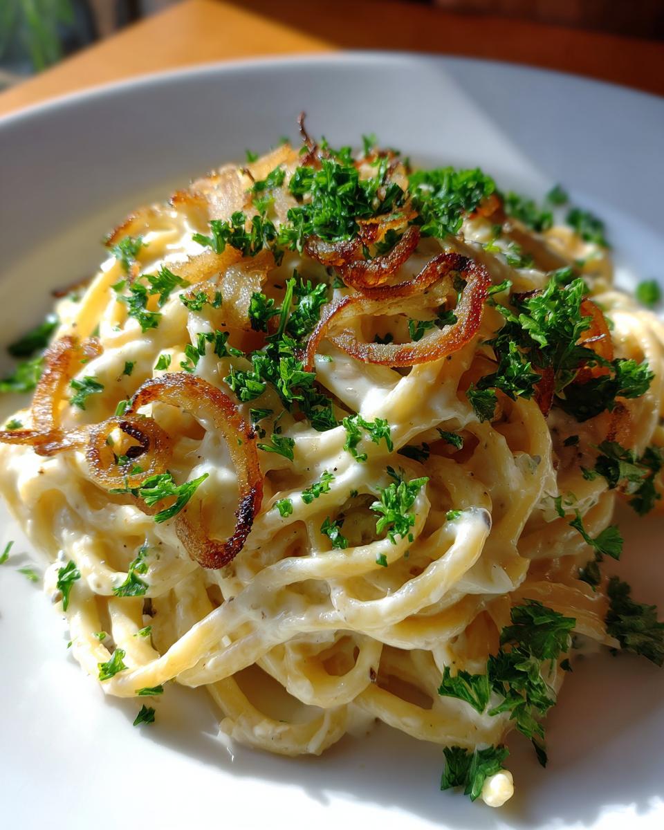 Nahaufnahme von Pasta mit Zwiebel-Sahnesauce, garniert mit knusprigen Röstzwiebeln und Petersilie.