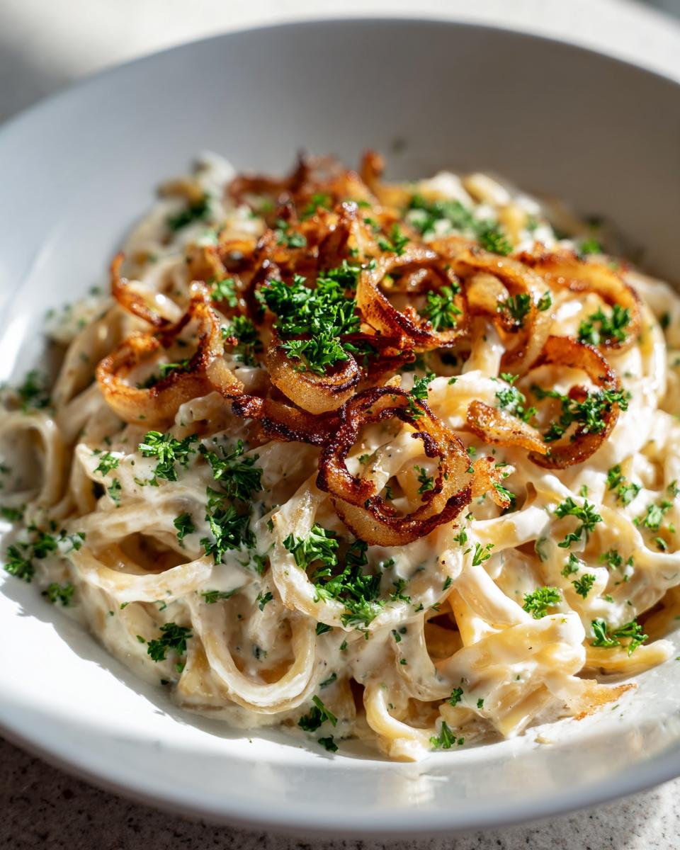 Nahaufnahme von Pasta mit Zwiebel-Sahnesauce, garniert mit knusprigen Röstzwiebeln und Petersilie.