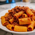 Nahaufnahme von Rigatoni mit Hackfleisch und Tomaten-Sahne Sauce auf einem weißen Teller.