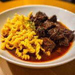 Nahaufnahme von saftigem Rindergulasch mit dunkler Soße und lockeren Spätzle.