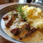 Nahaufnahme von saftigen Rinderstreifen in Pfefferrahmsoße, serviert mit lockerem Kartoffelstampf und Rosmarin.