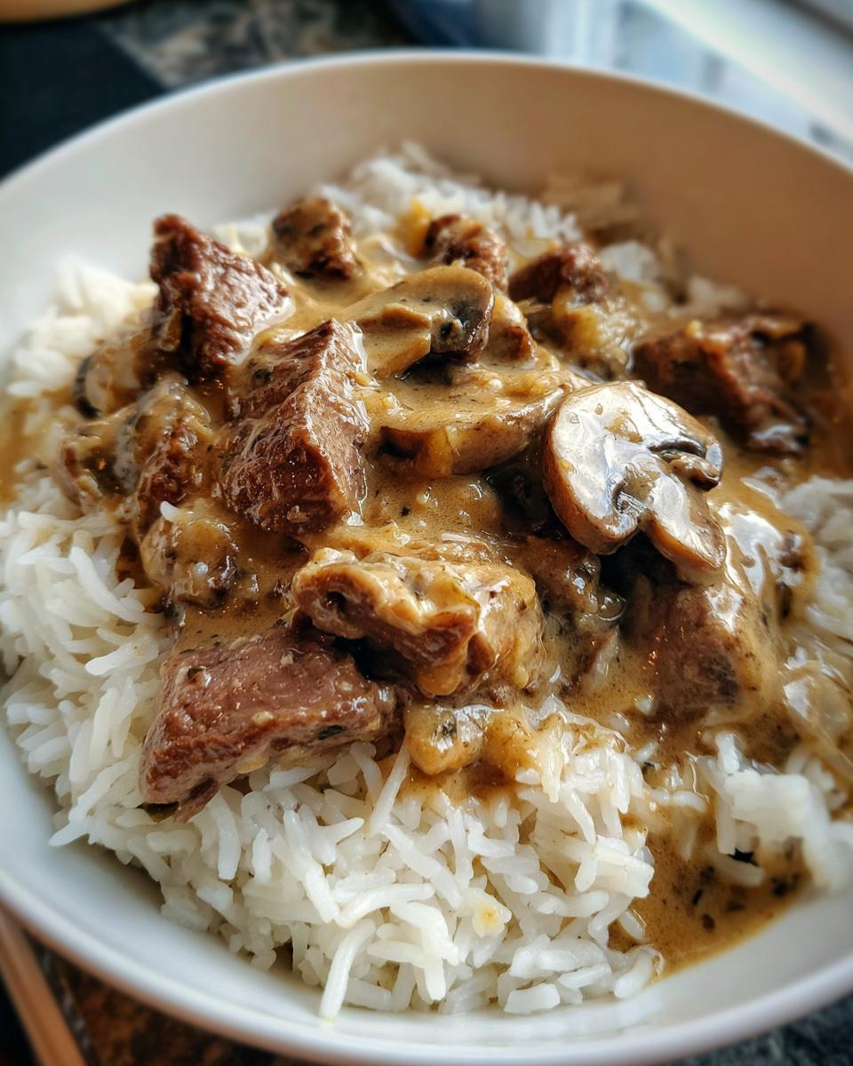 Ein Teller Russisches Stroganoff mit Reis, bedeckt mit cremiger Soße, Fleischstücken und Pilzen.