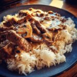 Nahaufnahme von cremigem Russisches Stroganoff mit Pilzen und Fleischstreifen auf lockerem Reis.