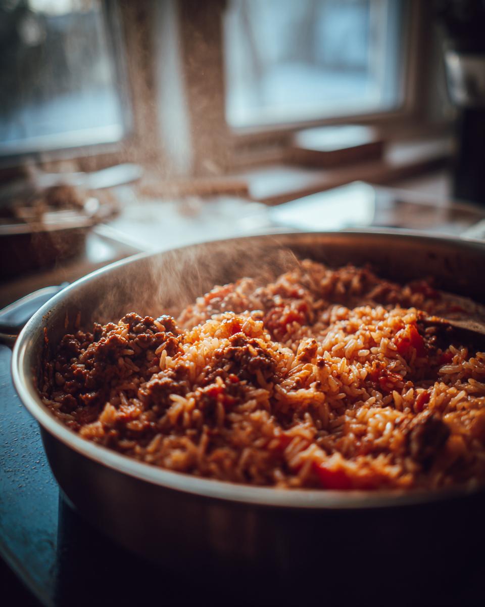 Nahaufnahme einer dampfenden Serbische Reis-Hackfleisch-Pfanne mit viel Hackfleisch und Reis in einer Metallpfanne.