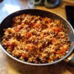 Eine appetitliche Serbische Reis-Hackfleisch-Pfanne mit viel Hackfleisch und Tomatenstücken in einer dunklen Pfanne.