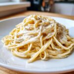 Nahaufnahme von cremigen Spaghetti mit Frischkäse und Knoblauch, bestreut mit schwarzem Pfeffer.