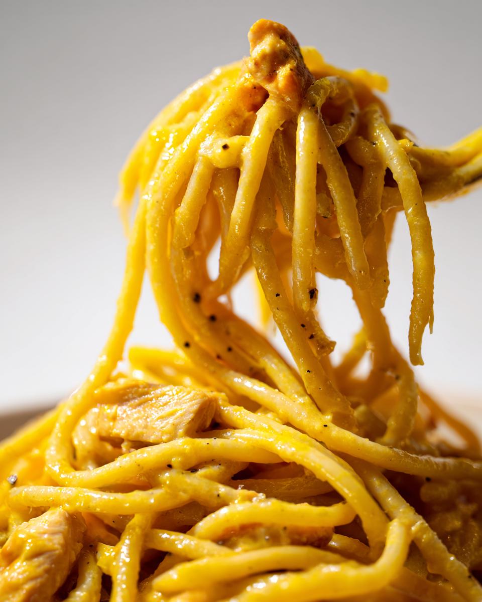 Nahaufnahme von Spaghetti mit Hähnchen in Zitronenrahm, die cremig und leuchtend gelb aussehen.