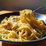 Nahaufnahme von Spaghetti mit Hähnchen in Zitronenrahm, wobei eine Gabel die cremigen Nudeln hochzieht.