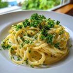 Nahaufnahme von cremigen Spaghetti mit Zitronen-Sahne, üppig garniert mit frischer Petersilie auf einem weißen Teller.