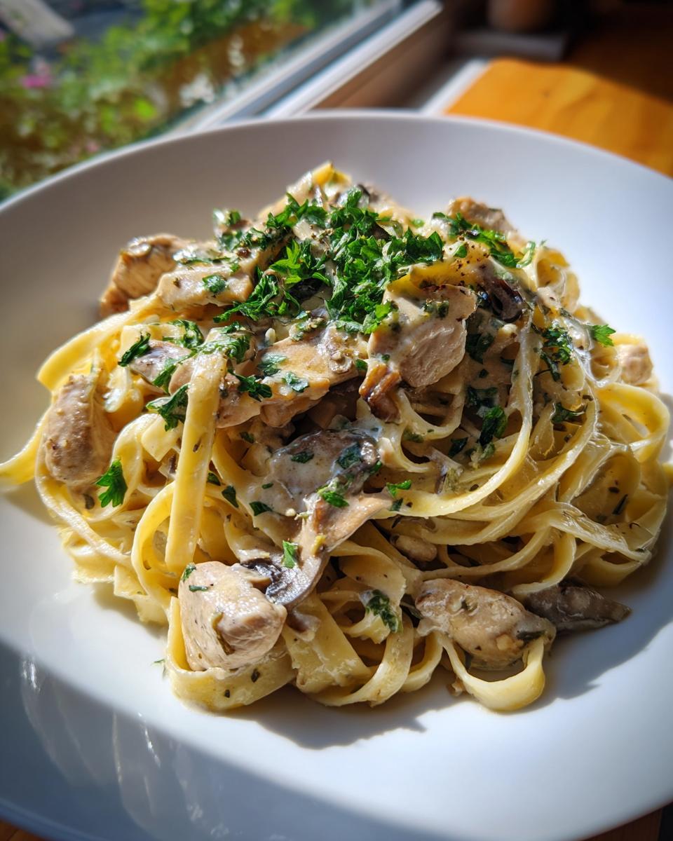 Teller mit cremigen Tagliatelle mit Hähnchen in Pilzrahm, garniert mit frischer Petersilie.