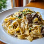 Nahaufnahme von cremigen Tagliatelle mit Steakstreifen in Pfefferrahmsoße, garniert mit Petersilie.