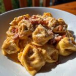 Nahaufnahme von cremigen Tortellini mit Schinken-Sahne, bestreut mit Parmesan und Pfeffer.