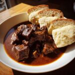 Nahaufnahme von Tschechischer Rindergulasch mit Knödeln in einer weißen Schüssel, appetitlich angerichtet.