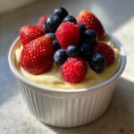 Ein cremiger Vanillepudding mit Beeren, garniert mit Erdbeeren, Himbeeren und Blaubeeren in einer weißen Schale.